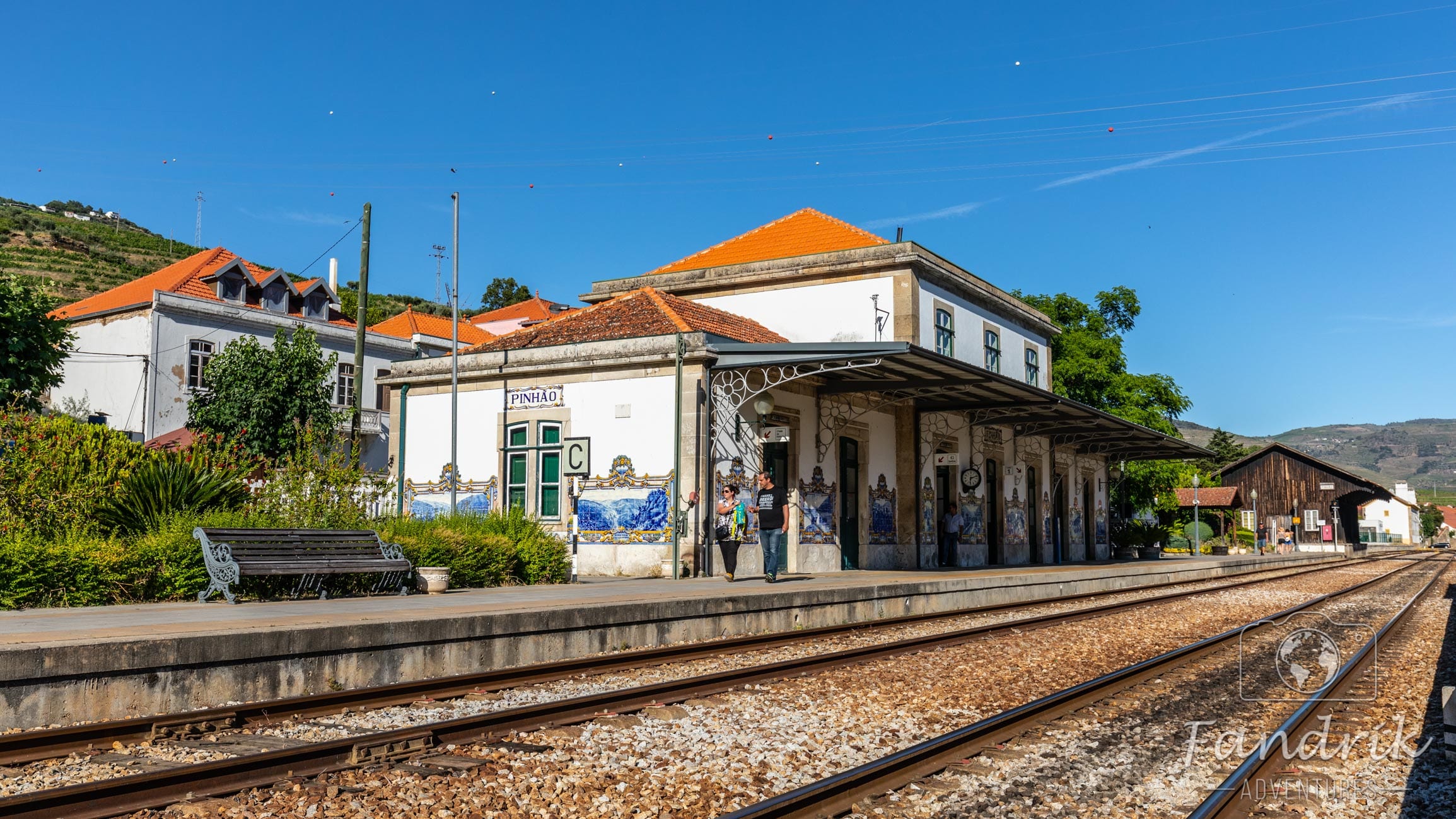 Weißes Bahnhofsgebäude mit rotem Dach und Gleise im Vordergrund