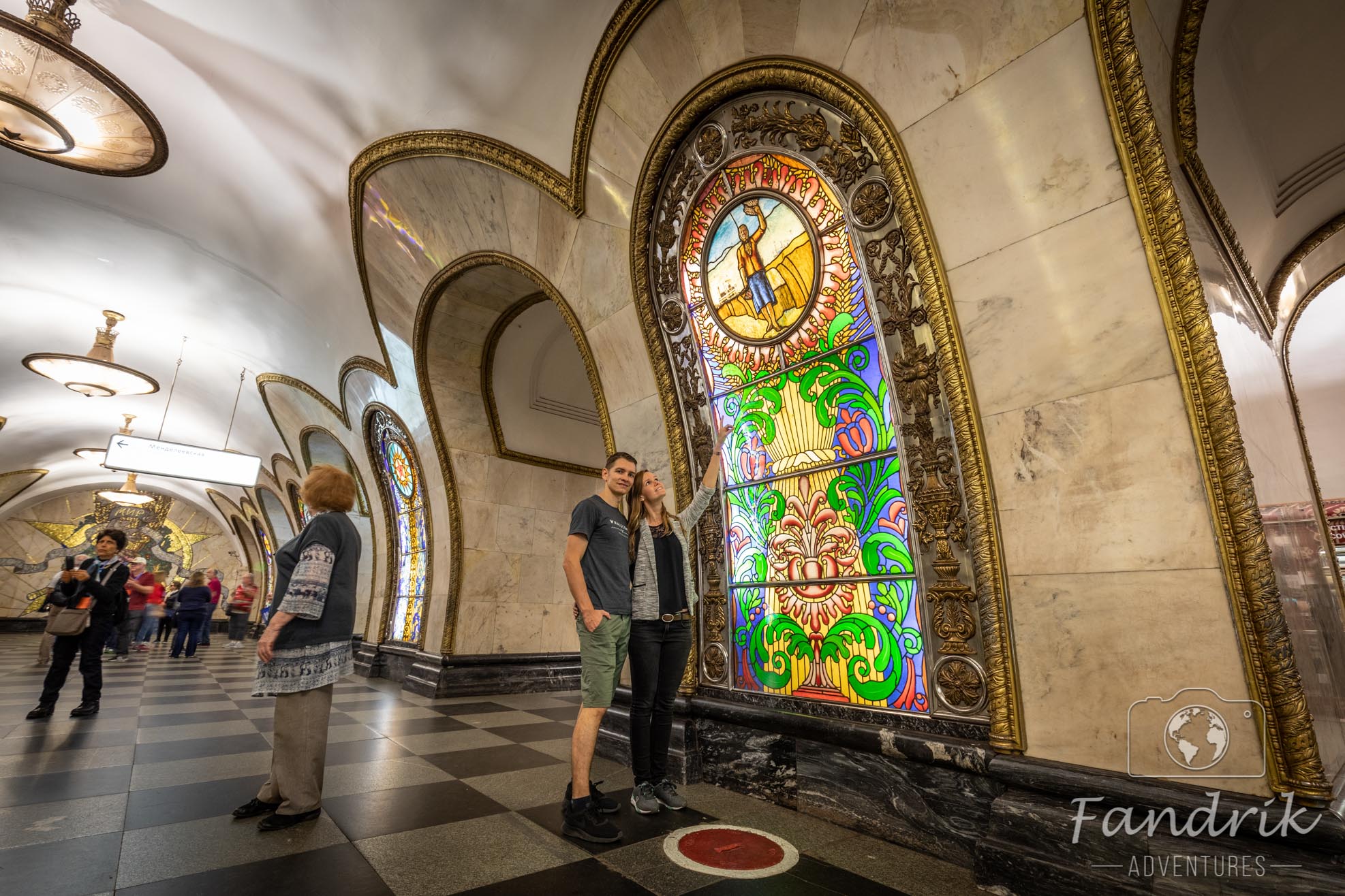 Zwei Personen stehen vor einem Glasmosaik in der Metro-Station Novoslobodskaya.