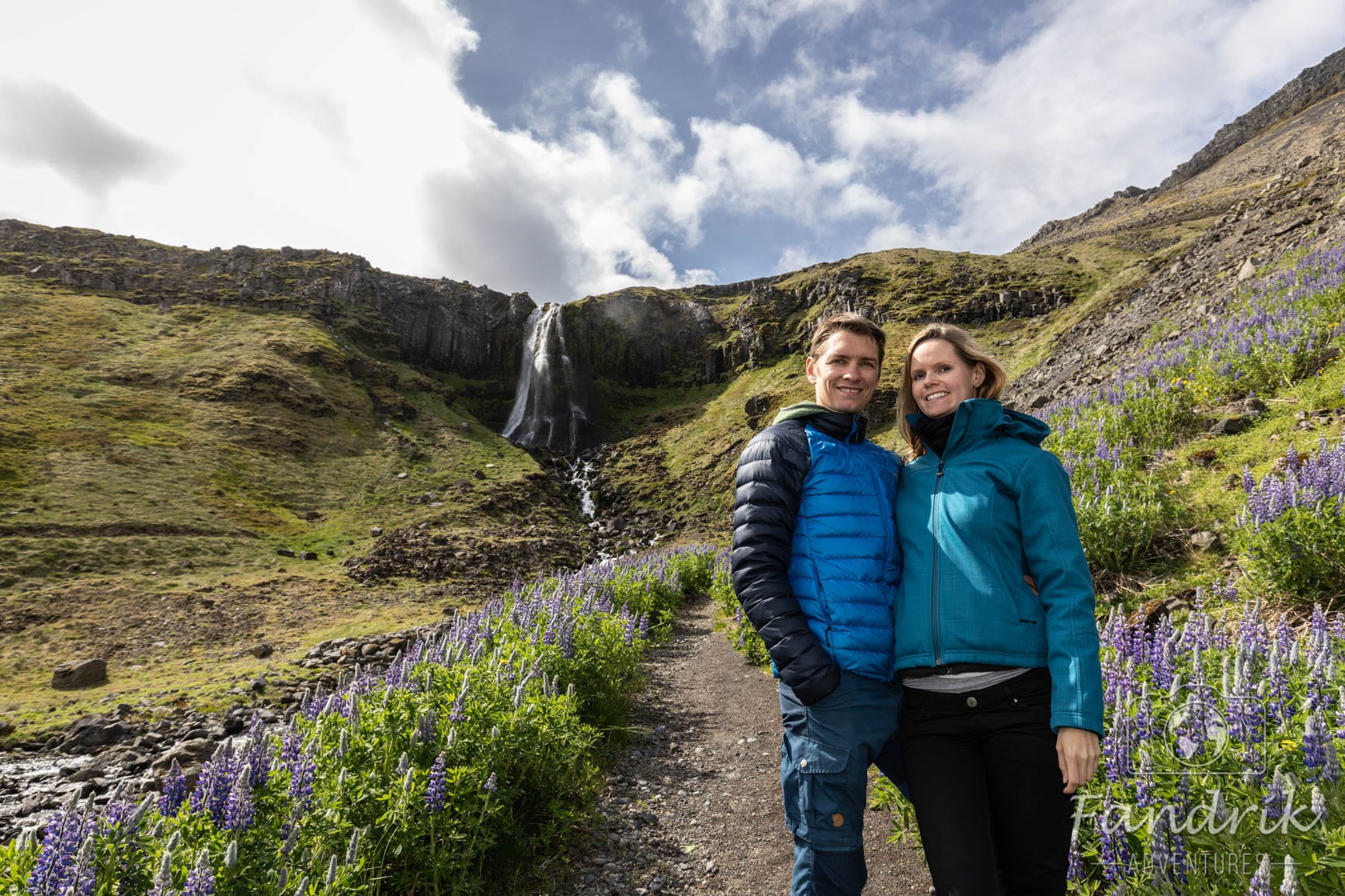 Zwei Personen stehen vor dem Wasserfall in Olafsvik.